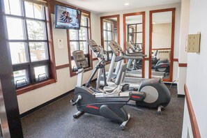 A gym with cardio equipment, large windows, and mirrors.
