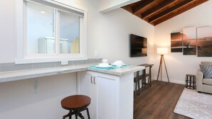 A modern kitchen with white cabinets, a large window, and a wooden ceiling.