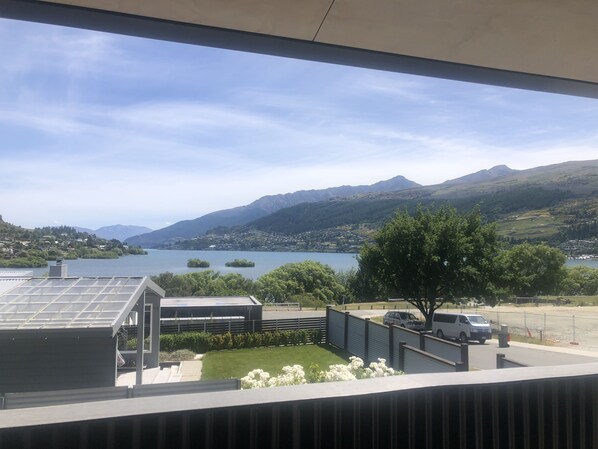 Vista desde una ventana sobre un lago, montañas y un estacionamiento con un coche blanco.