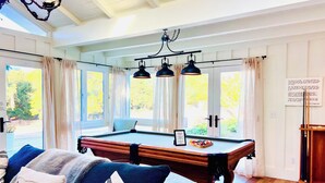 Una habitación acogedora con una mesa de billar, un sofá con cojines decorativos y una lámpara de araña.