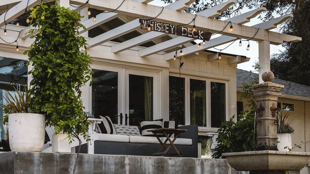 Un área de estar al aire libre con techo, un letrero que dice "Whiskey Deck", una jardinera de concreto y una fuente de piedra.