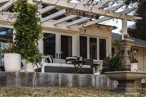 Un espace extérieur abrité, aménagé avec des sièges, sur lequel on peut lire l’inscription « Whiskey Deck », ainsi qu’un bac à plantes en béton et une fontaine en pierre.