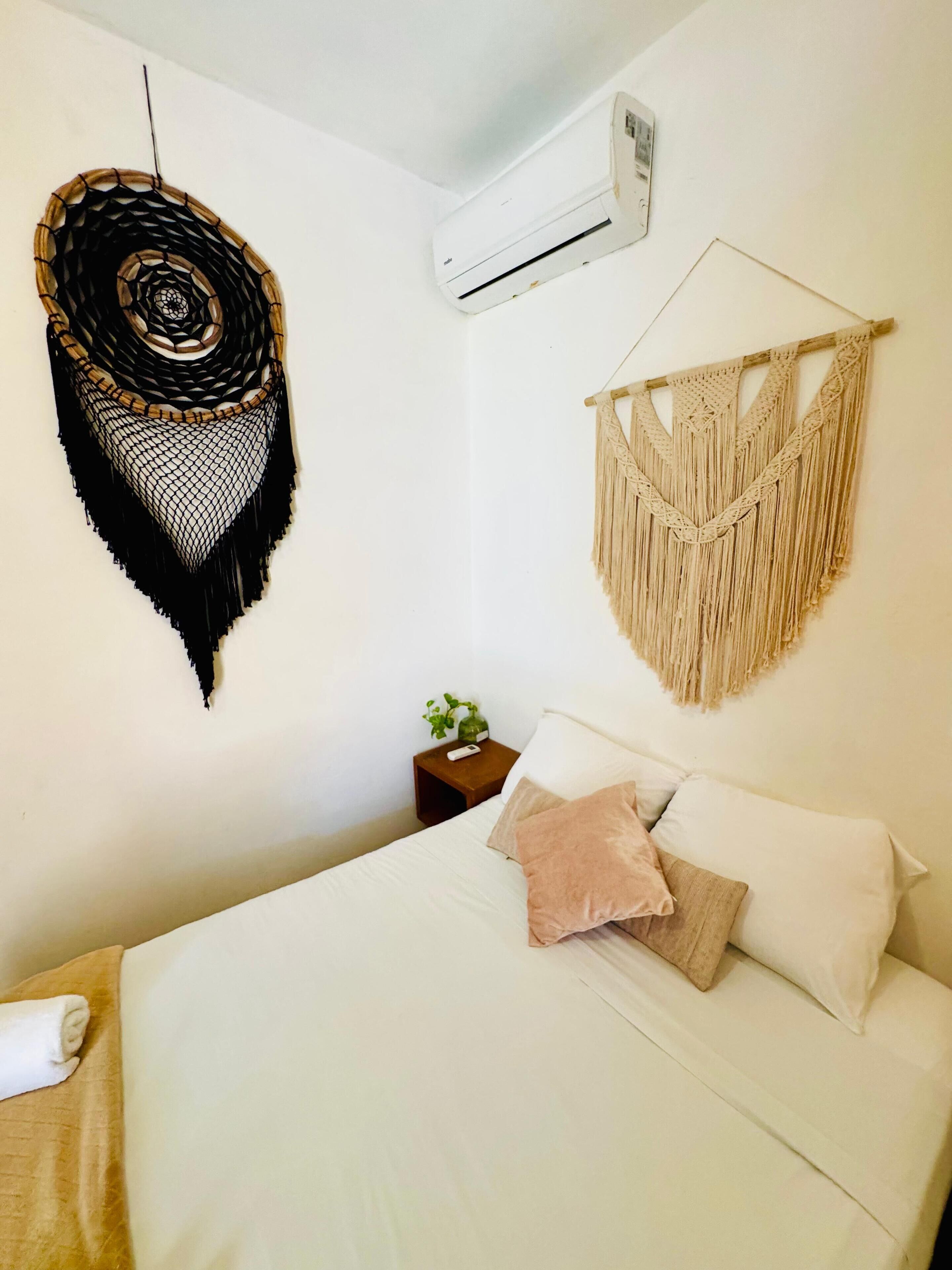 Ein Schlafzimmer mit einem Bett, einer wandmontierten Klimaanlage, einem Makramee-Wandbild und einem gewebten Wandbehang.