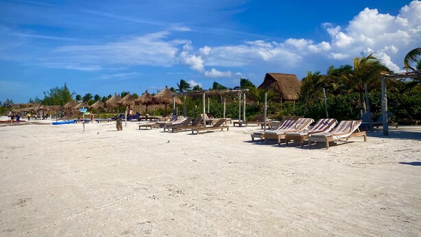 A beach with thatched-roof huts, lounge chairs, and palm trees. - AKBAL Holbox (Isla Holbox)