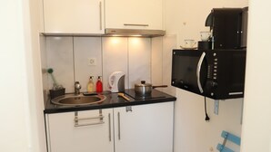 Une cuisine de taille réduite équipée d’un évier, d’une cuisinière, d’un four à micro-ondes et de placards.