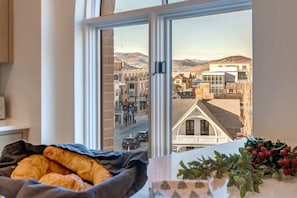Janela com vista para uma cidade, cama com cobertor e mesa com uma planta.