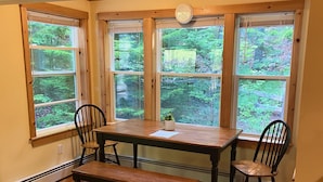 Un comedor con mesa y sillas de madera, ventanas amplias con vistas a zonas verdes y un calentador empotrado.