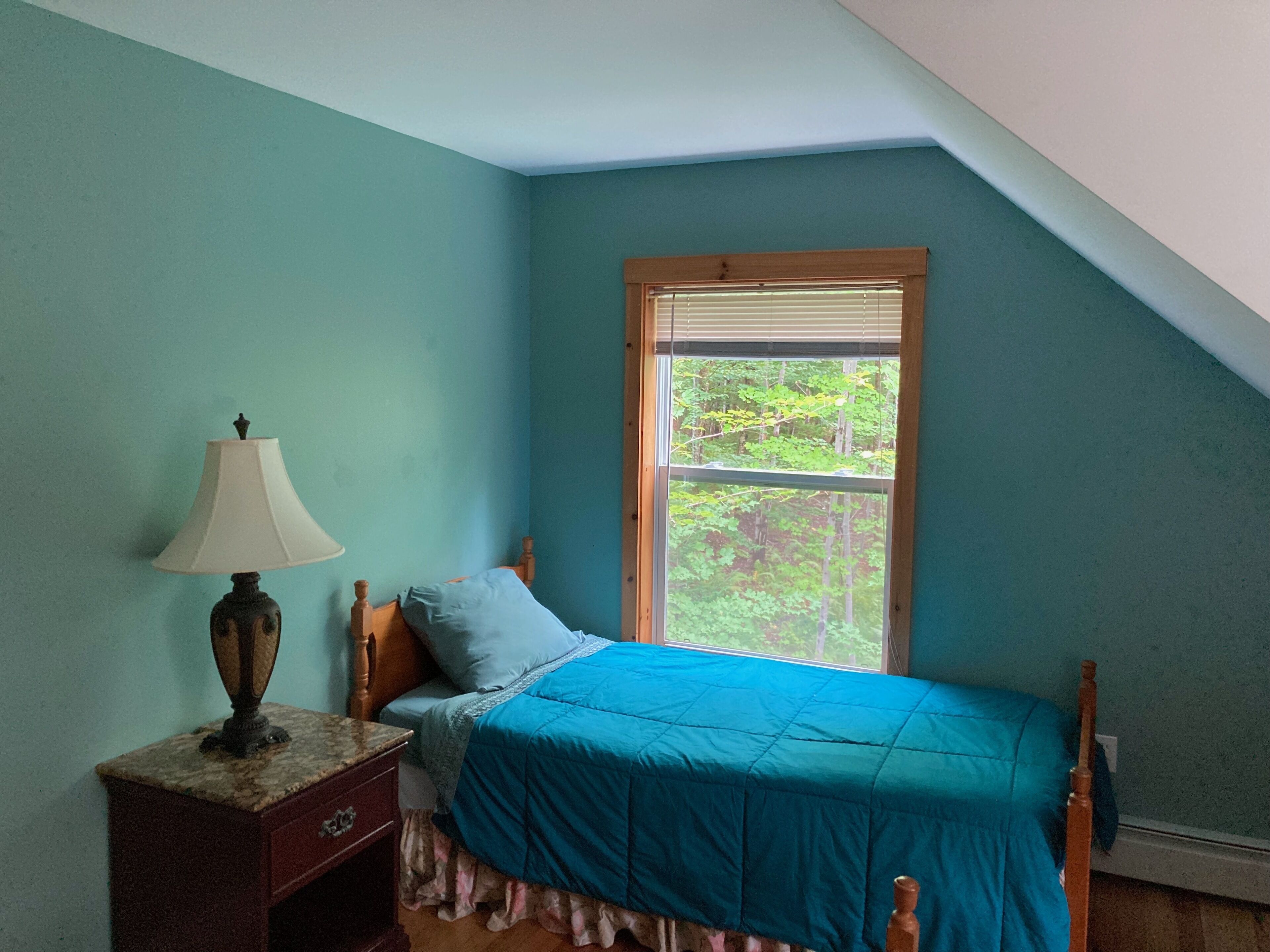 A bedroom with a bed, a nightstand, a lamp, and a window with a view of trees.