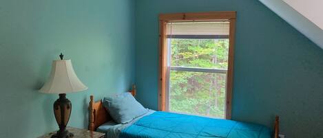 A bedroom with a bed, a nightstand, a lamp, and a window with a view of trees.