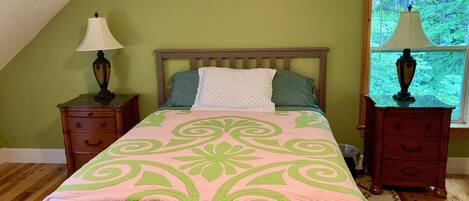 A bedroom with a bed, two nightstands, a window, and a view of greenery outside.