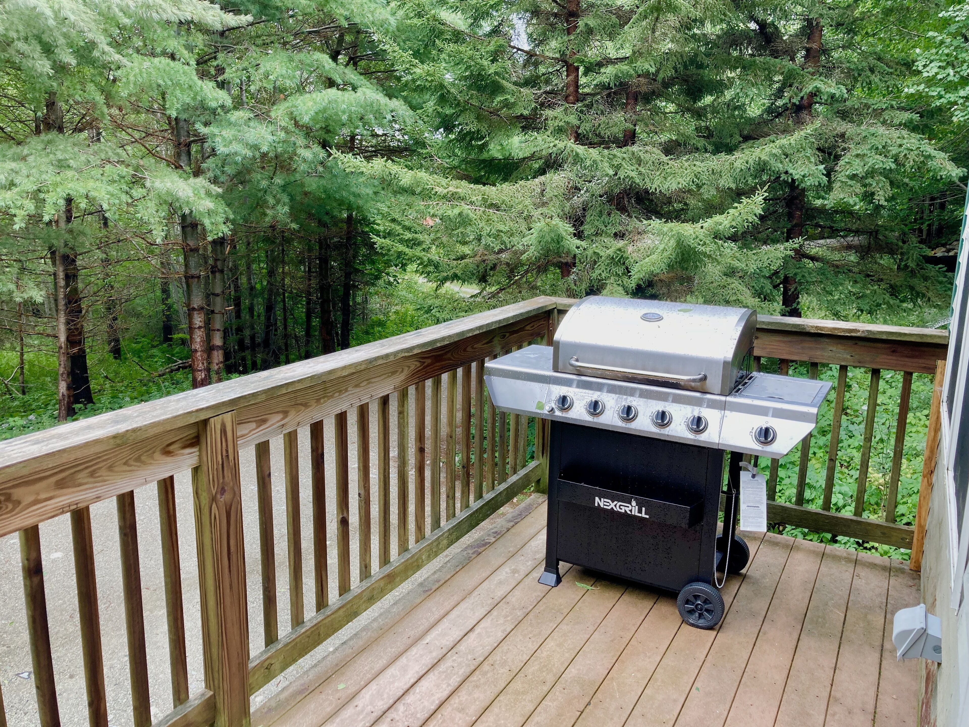 A barbecue grill on a wooden deck with a view of a forest.