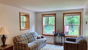 Una habitación con un sofá a cuadros, una mesita con un florero y vistas a un jardín trasero a través de amplias ventanas.