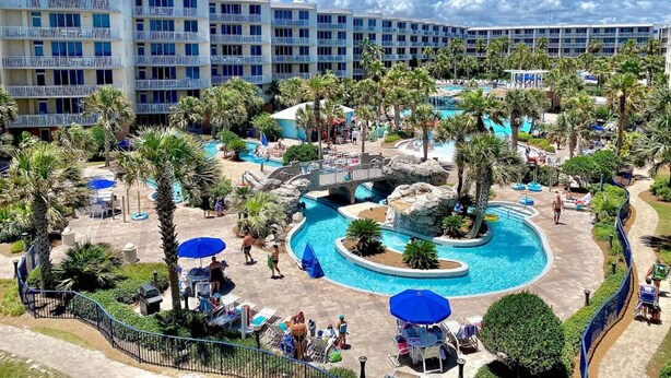 Un hôtel doté de nombreux balcons, d’une piscine centrale agrémentée d’une cascade et entouré de palmiers.