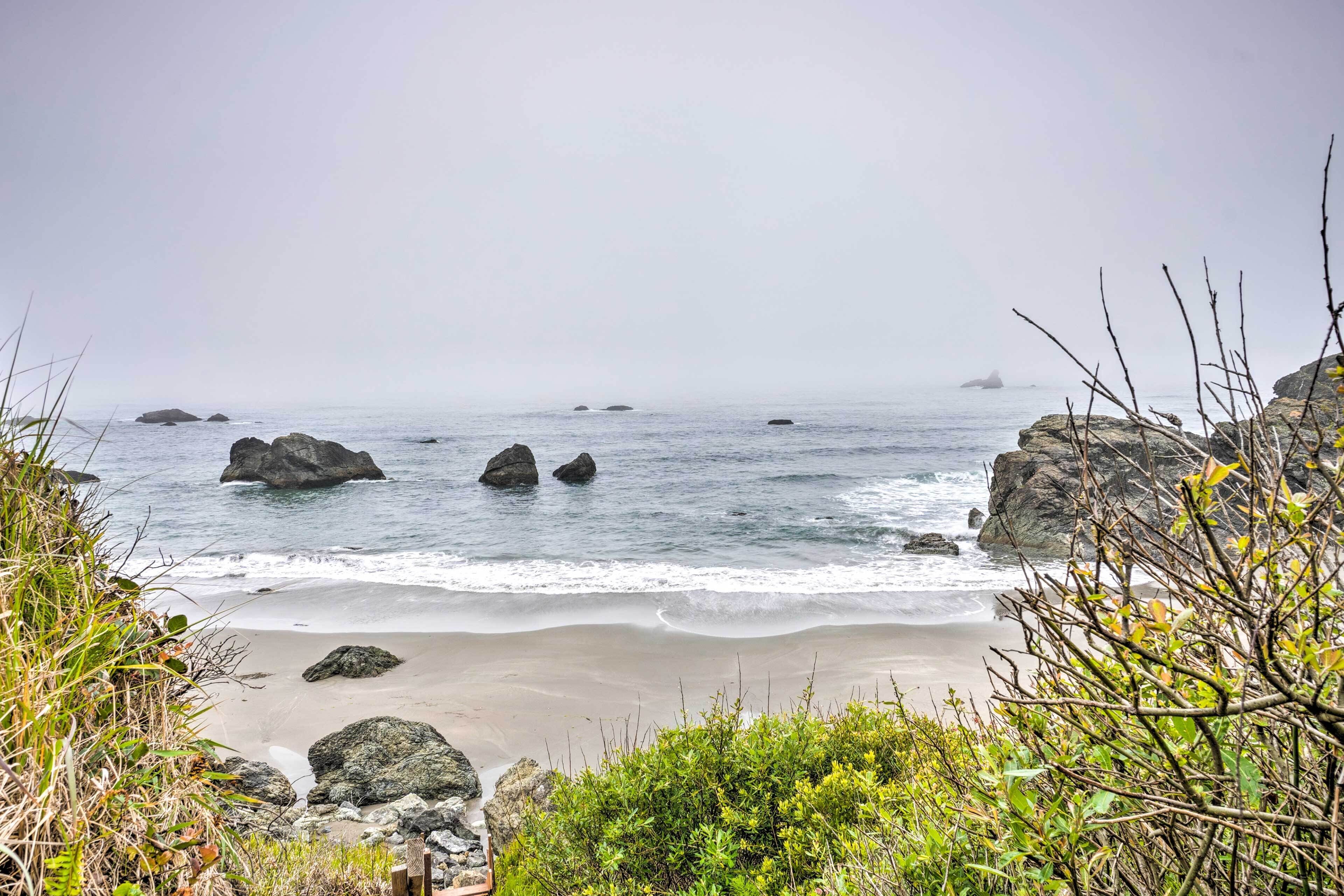 A coastal beach scene with large rocks and vegetation.