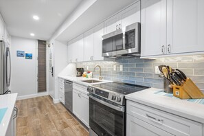 A modern kitchen with stainless steel appliances, a tiled backsplash, and wooden flooring. - Ground Floor Garden Studio - Kaanapali Villas B143 (Lahaina)