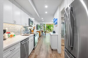 A modern kitchen with stainless steel appliances, white cabinetry, and a view into the dining area.