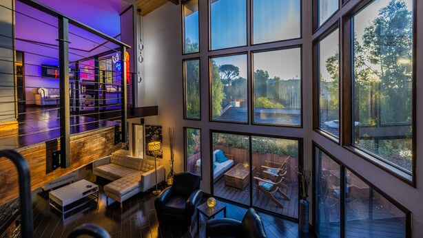 Ein großzügiger Wohnbereich mit großem Fenster und Blick auf eine Terrasse, eine gemütliche Sitzecke mit Sofa und Sesseln sowie ein modernes Design mit freiliegenden Holzbalken.