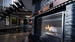 Ein modernes Wohnzimmer mit Kamin aus Stein, dunklem Holzboden und einer Treppe mit Metallgeländern.