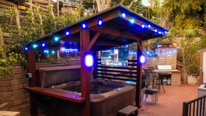 Ein Bereich mit Whirlpool, einer hölzernen Pergola und Lichterketten, umgeben von Ziegelmauern und Blumentöpfen.