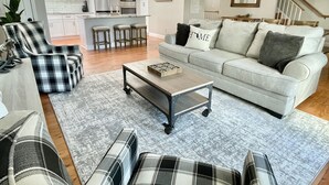 A modern living room with a sofa, chairs, and a coffee table. There is a kitchen in the background with white cabinets and a refrigerator. - Luxury Ocean View Getaway! (Jacksonville Beach)