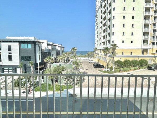Un edificio residencial de varios pisos con balcones, un área de estacionamiento y vista al océano.