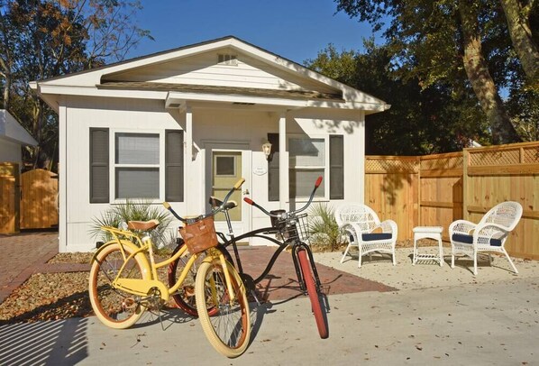 Une petite maison blanche avec un porche, un vélo jaune et des chaises en osier blanc.