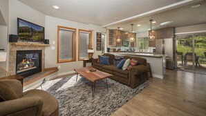 Una sala de estar moderna con chimenea, un sofá, una mesa de centro y una zona de cocina con refrigerador y armarios.