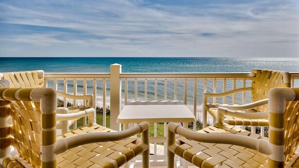 Ein Balkon mit Korbstühlen und einem Tisch mit Blick auf einen Strand.