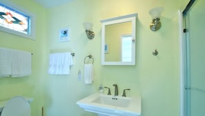 Un baño con inodoro blanco, lavamanos sobre pedestal, espejo y ventana con diseño de vitral.
