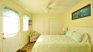 Un dormitorio con cama, ventilador de techo, ventana con cortinas y puerta.