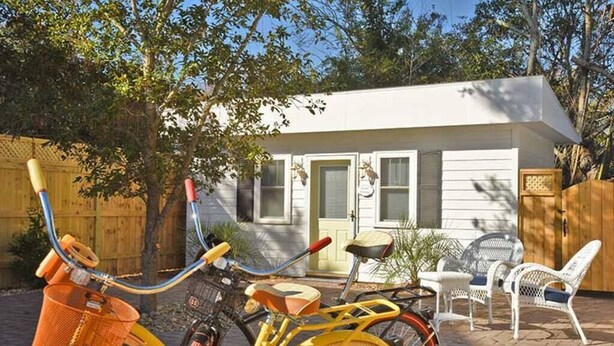 Una casita blanca con un porche, una bicicleta y una silla.