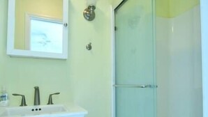 Un baño con lavamanos pedestal blanco, cabina de ducha con mampara de vidrio y espejo sobre el lavamanos.