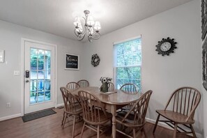 A dining room with a wooden table and chairs, a chandelier, a window with blinds, a clock, and a welcome sign.