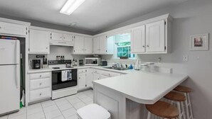 Une cuisine moderne avec des meubles blancs, un îlot central doté de tabourets, un four encastré, un four à micro-ondes et un évier.
