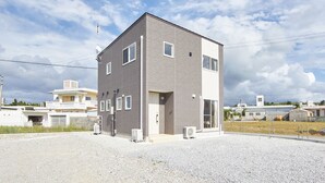 Um edifício moderno de dois andares com telhado plano, uma pequena varanda e uma porta com painel de vidro.