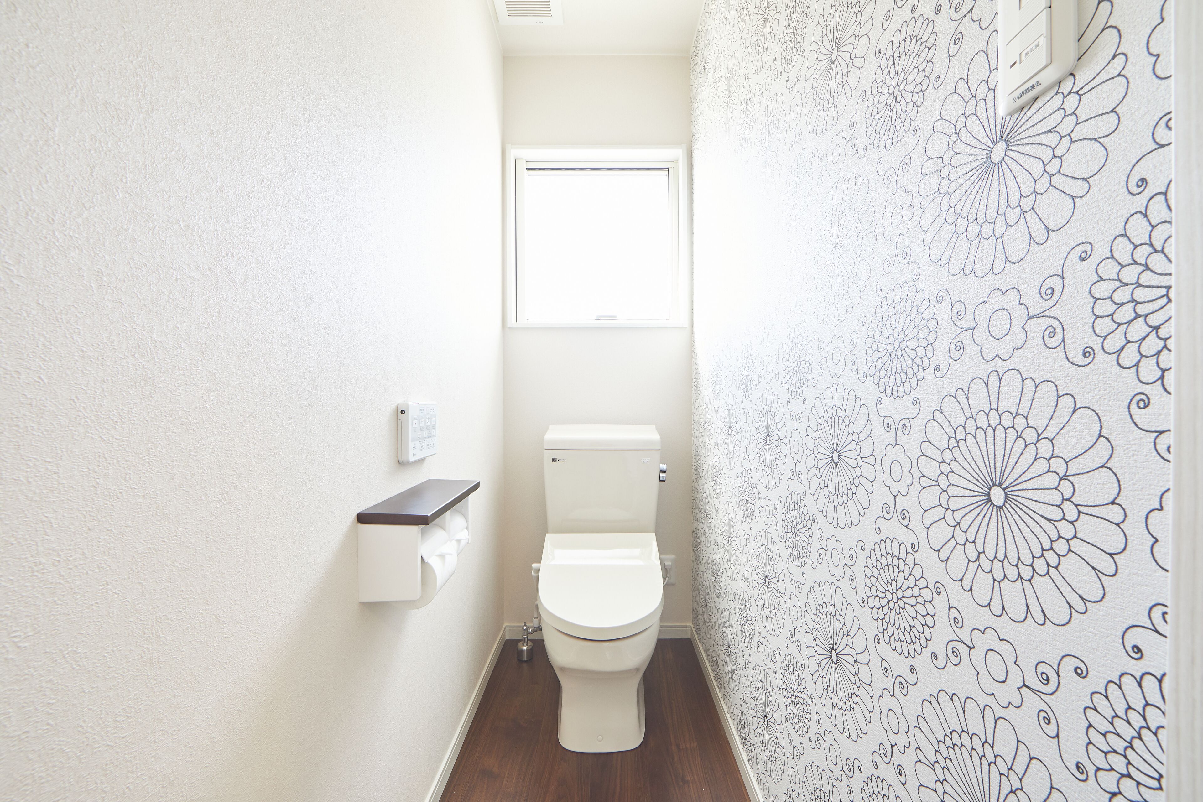 A small, narrow bathroom with a toilet, a window, and a wall-mounted shelf.