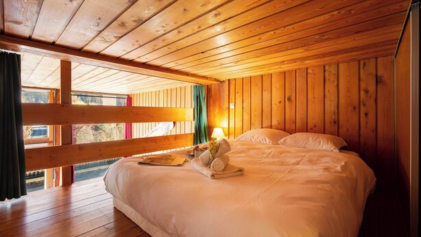 Un dormitorio de cabaña de madera con una cama, una ventana con cortinas y un techo de madera.