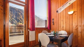 Un interior de madera con una mesa de comedor dispuesta para dos personas, una ventana con cortinas y una tabla de snowboard apoyada contra la pared.