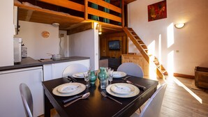 Comedor con una mesa de madera para cuatro personas, cocina al fondo y dormitorio en un altillo.