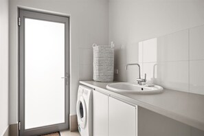 A modern bathroom with a washing machine, a sink, and a striped basket.