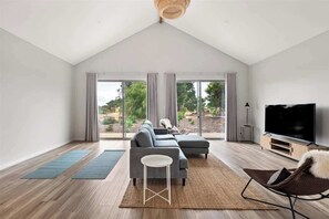 A modern living room with a large sectional sofa, a flat-screen TV, and a large window with curtains.