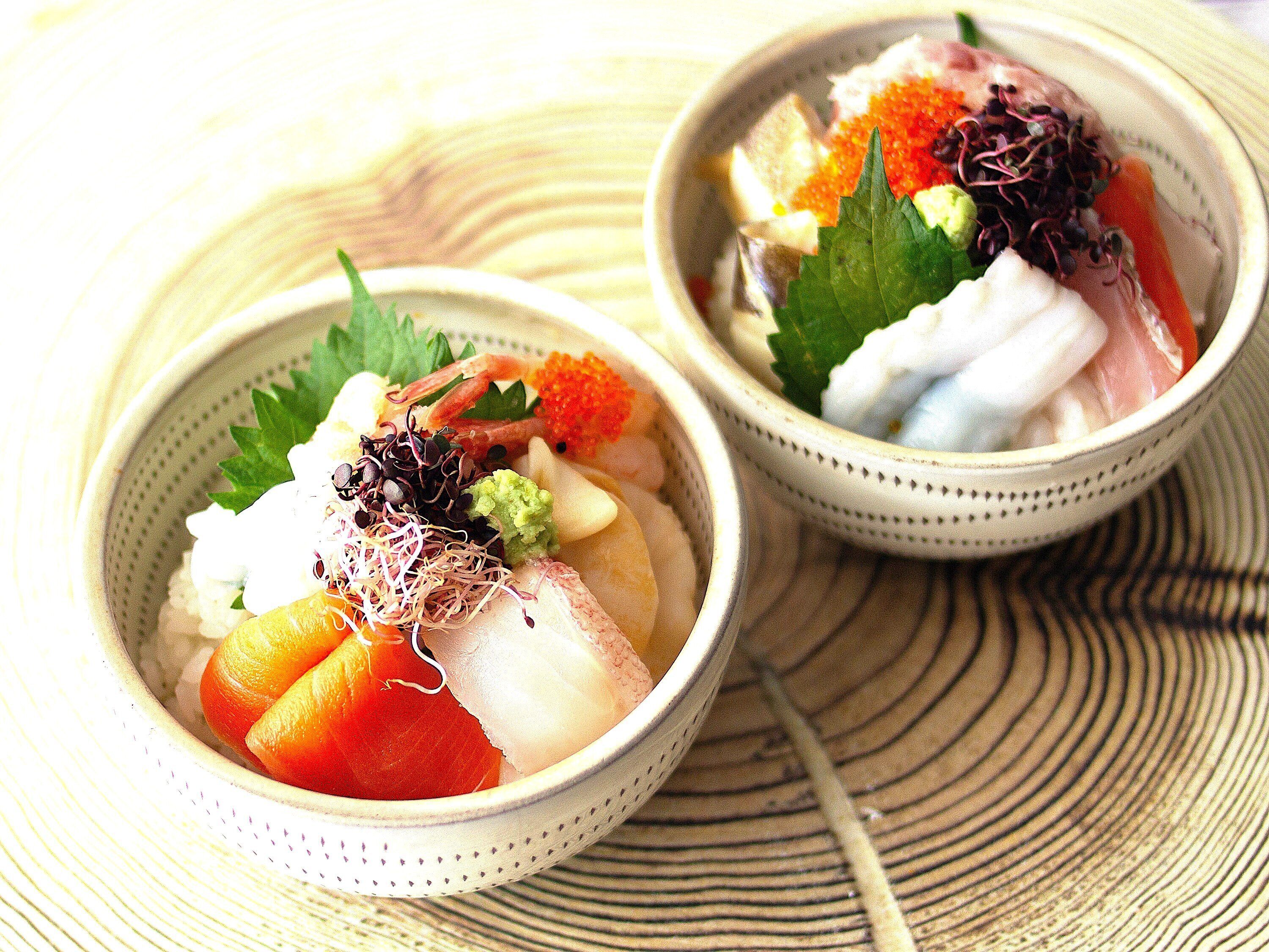 Two bowls of sashimi with various toppings on a woven mat.