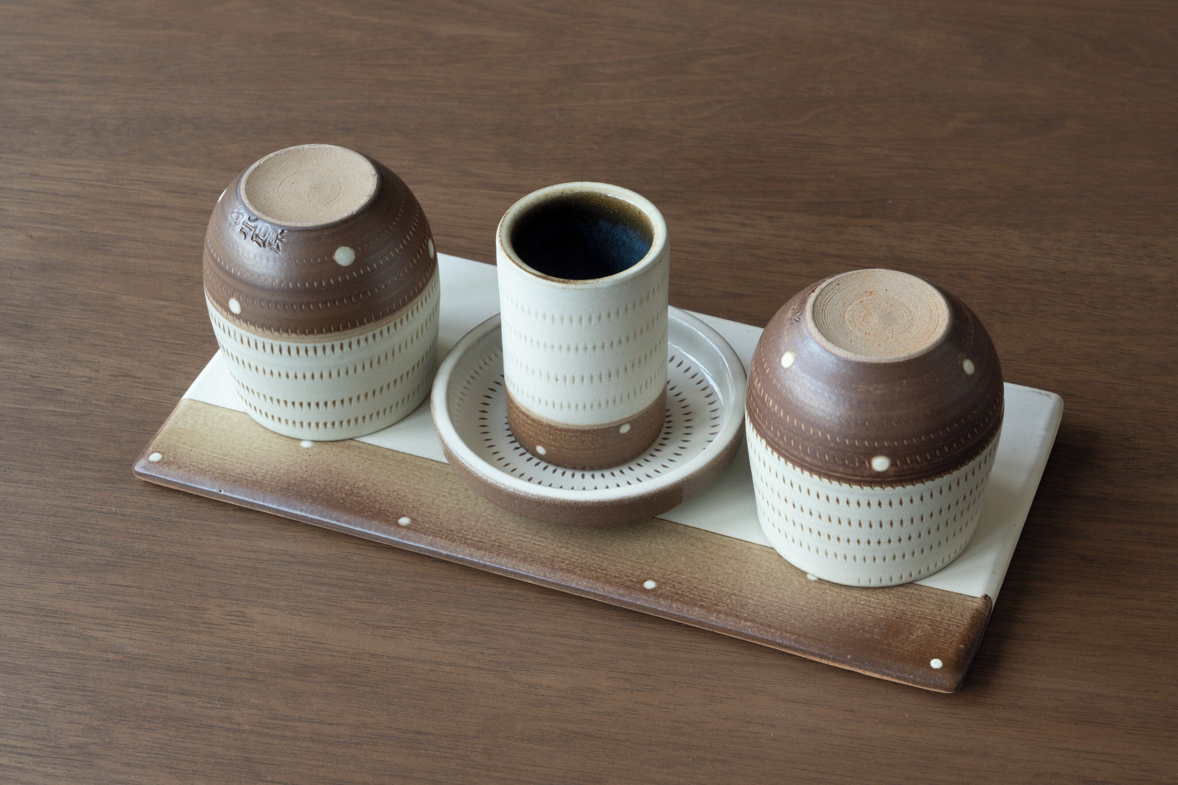 A set of three ceramic cups and saucers on a wooden tray.