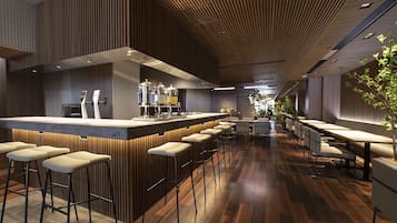 A modern bar area with a long counter, multiple stools, and a seating area with tables and chairs.