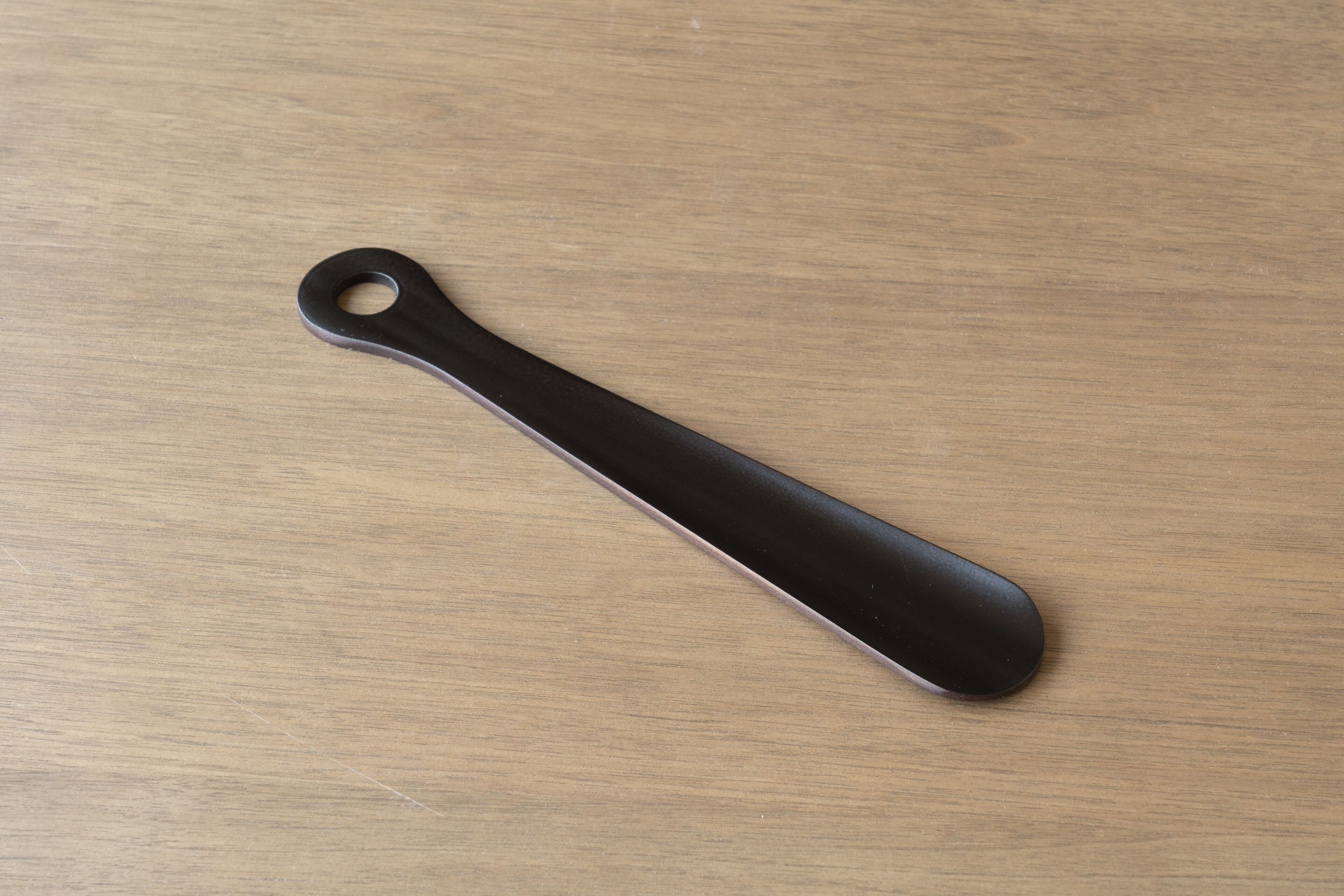 Un objet noir, plat et allongé, doté d’un trou circulaire à une extrémité, reposant sur une surface en bois.