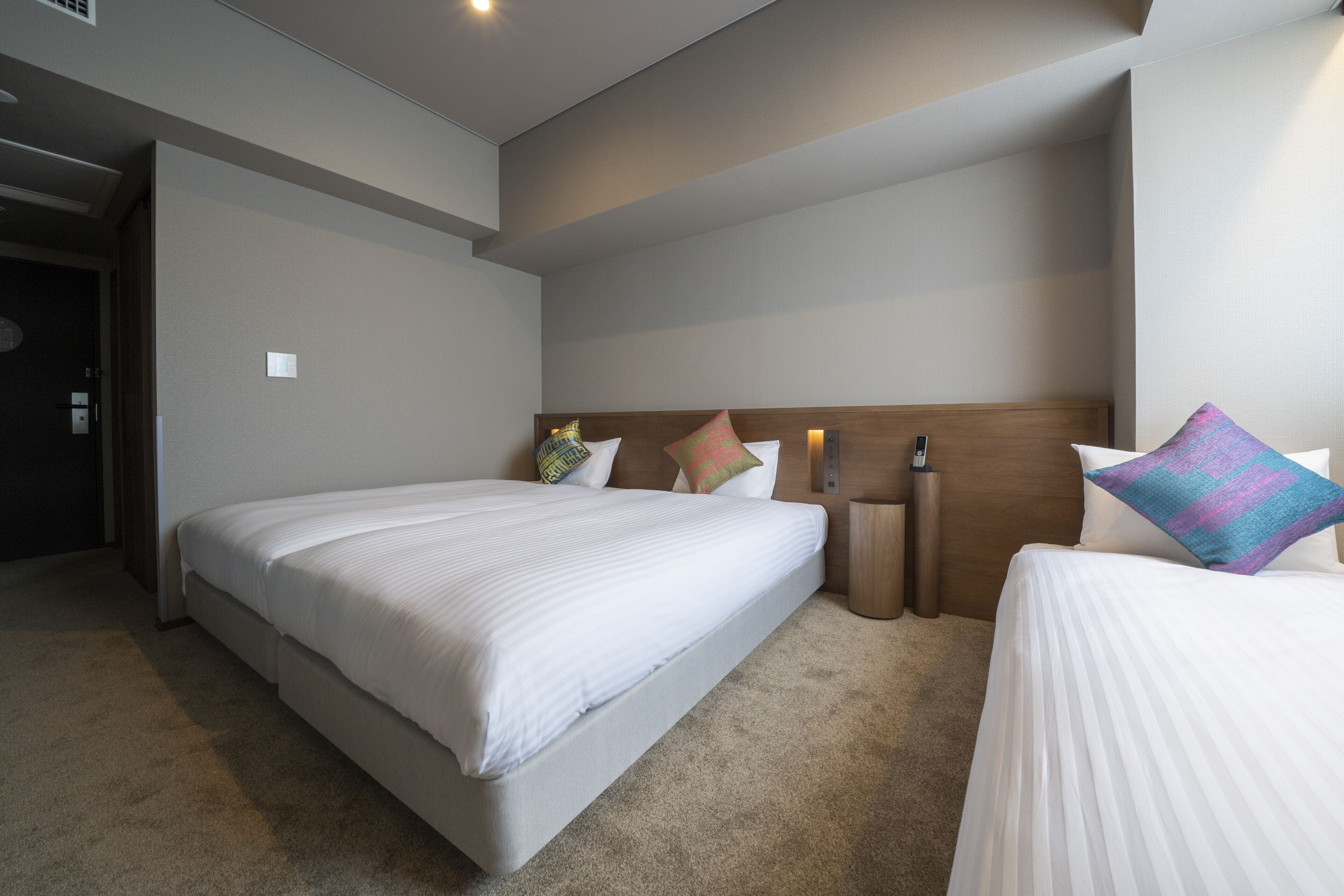 A hotel room with a large bed, a smaller bed, a nightstand, and a bedside table.