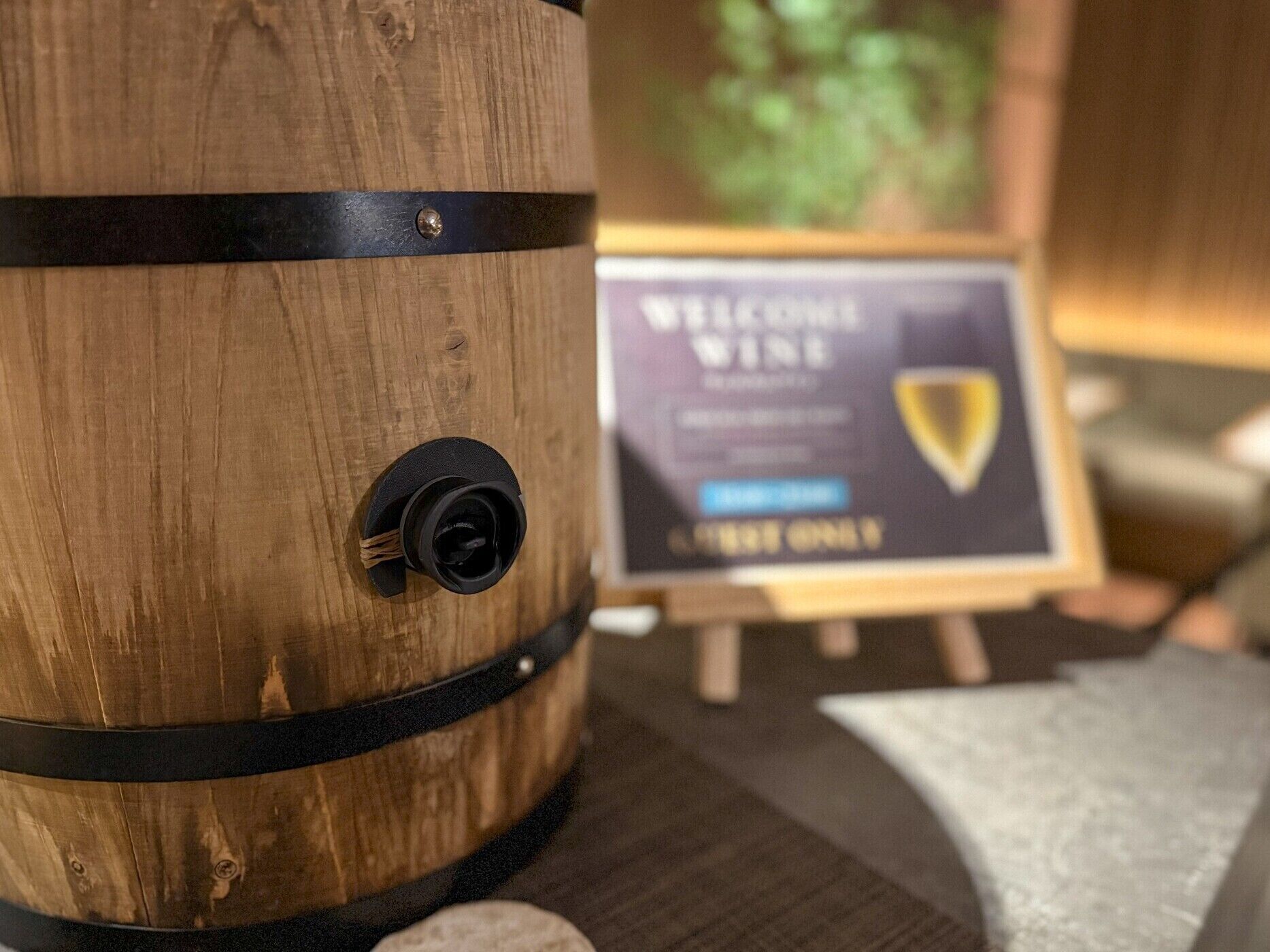 A wooden barrel with a black strap and a label that reads "WELCOME WINE".