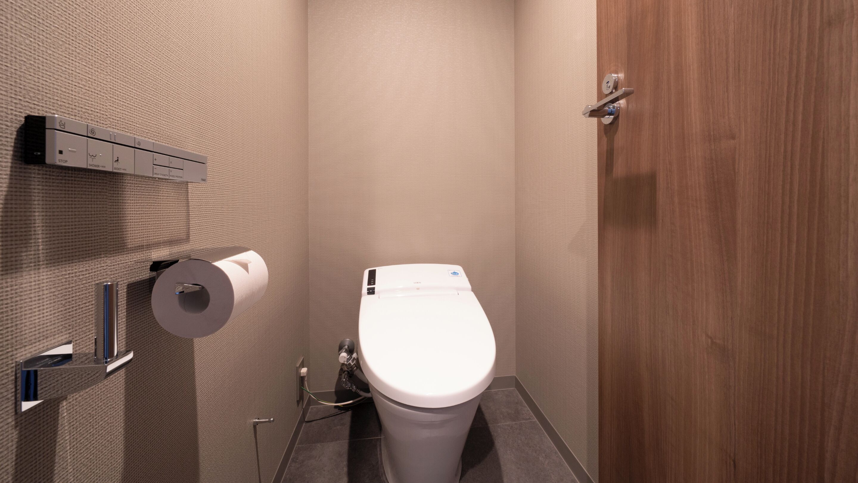 A modern bathroom with a toilet, paper dispenser, and a wooden door.