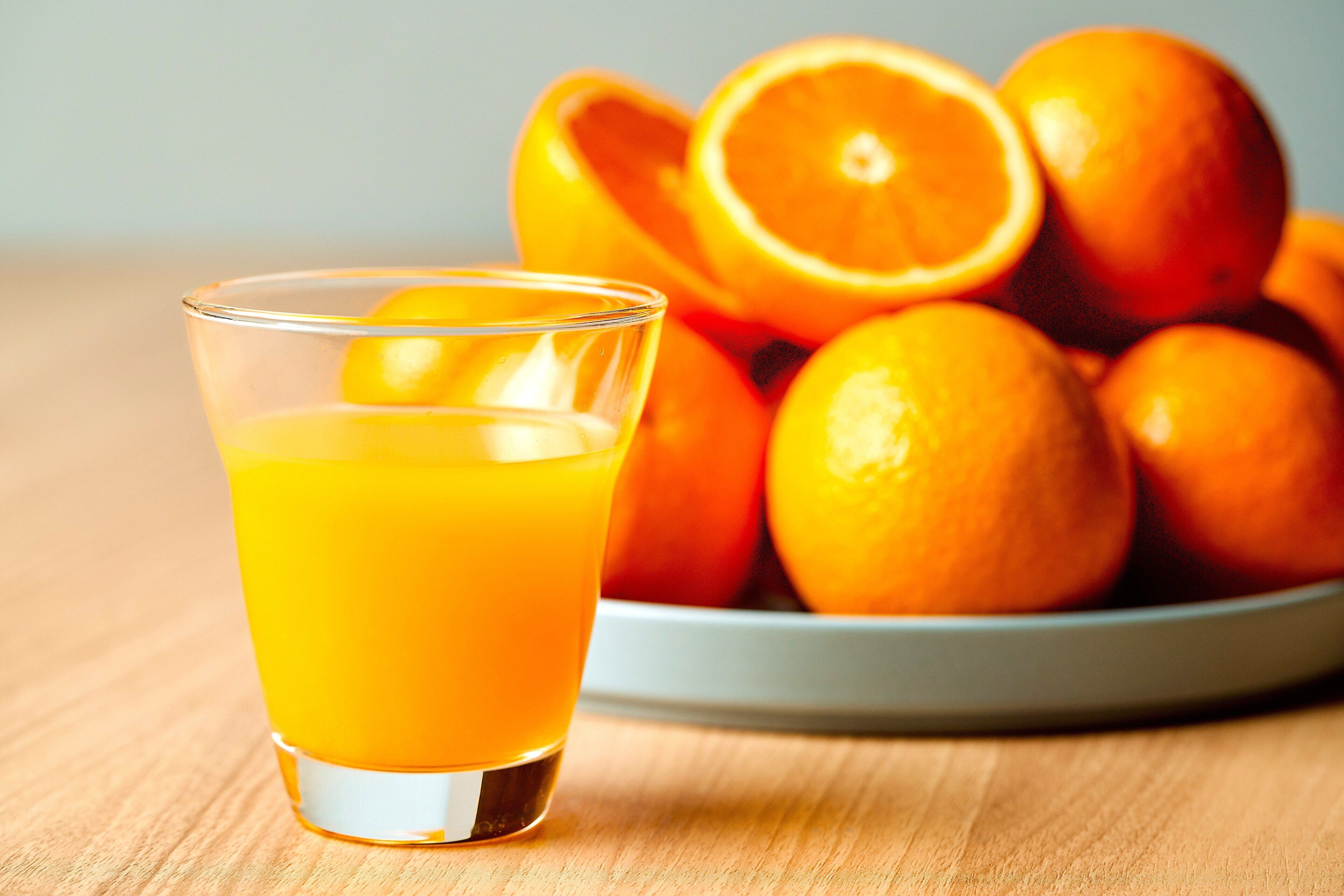 A glass of orange juice and a bowl of oranges on a wooden table.