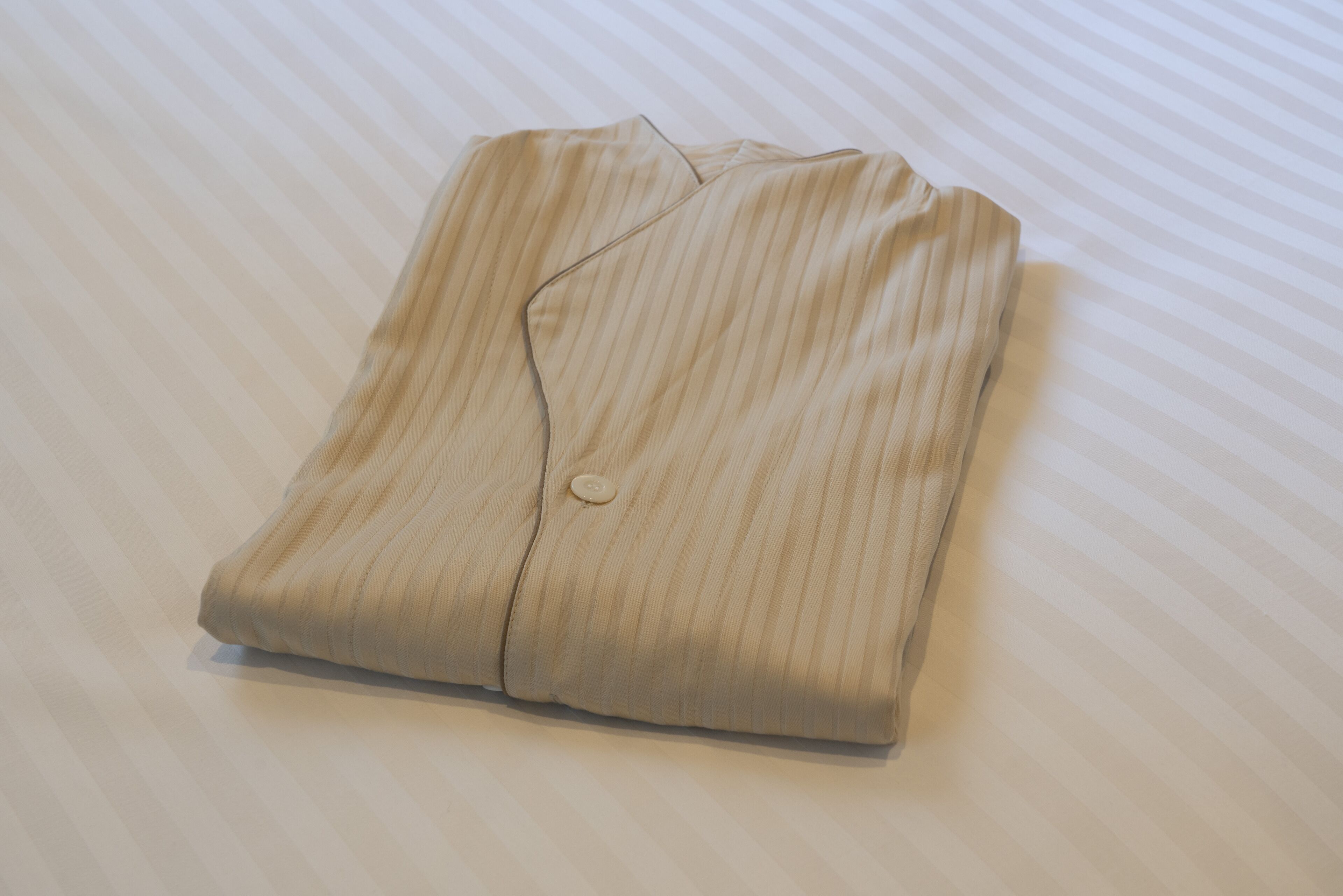 A neatly folded beige shirt with a button on a striped bedspread.